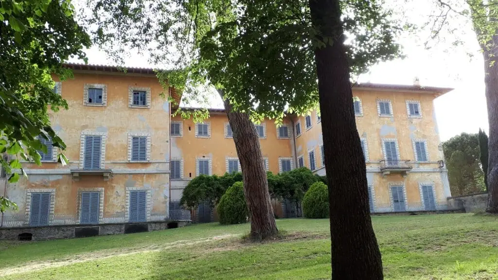 Villa storica gialla con giardino e alberi.