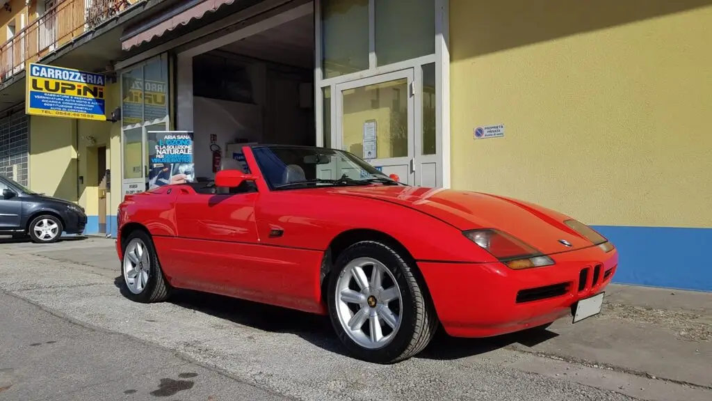 Auto sportiva rossa parcheggiata davanti a edificio giallo.