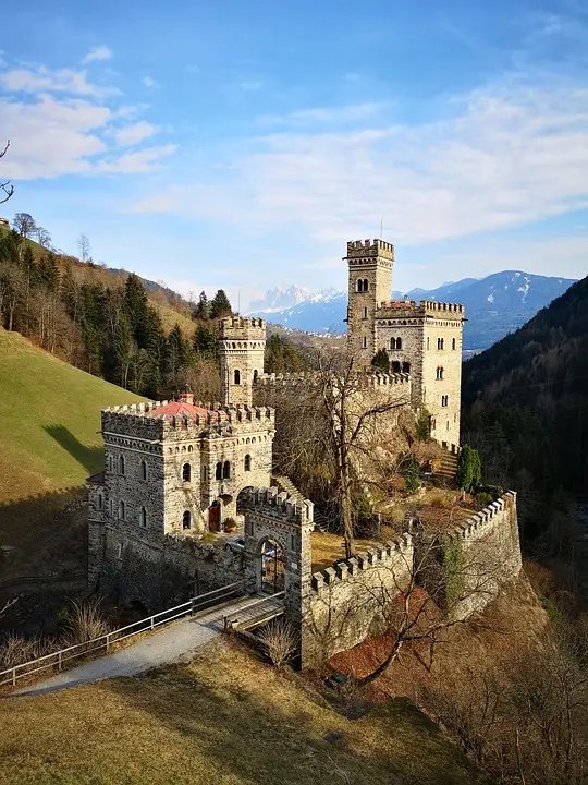 Castello medievale tra montagne verdi, cielo azzurro.