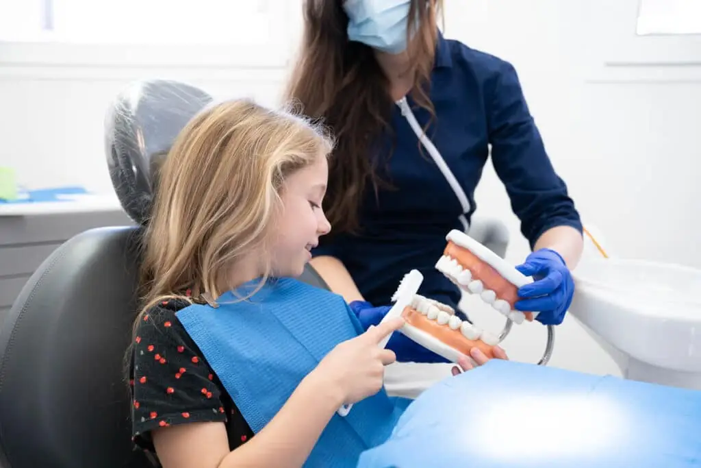 Bambina apprende igiene dentale in studio dentistico.