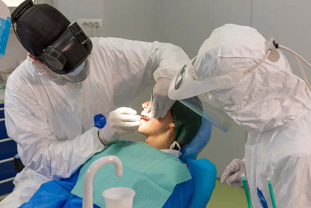 Dentista in tuta protettiva esamina paziente.