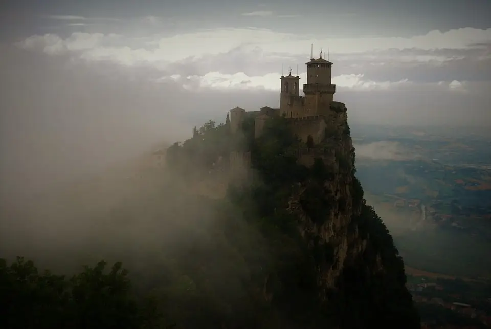 Castello nebbioso su promontorio roccioso.