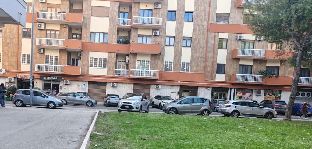 Condominio urbano con negozi e parcheggio antistante.