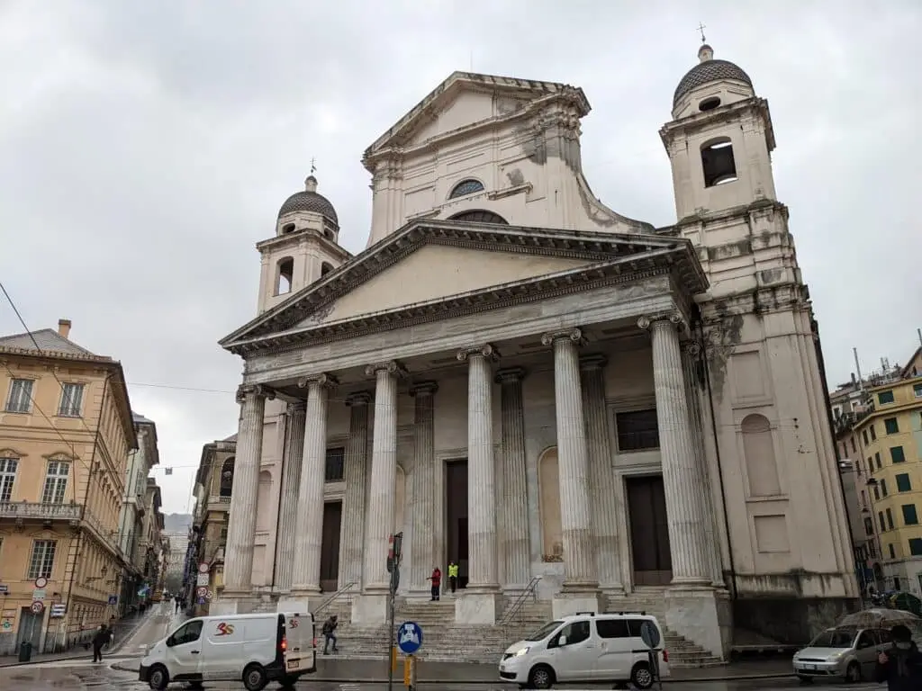 Chiesa storica con colonne, veicoli e persone, giorno nuvoloso.