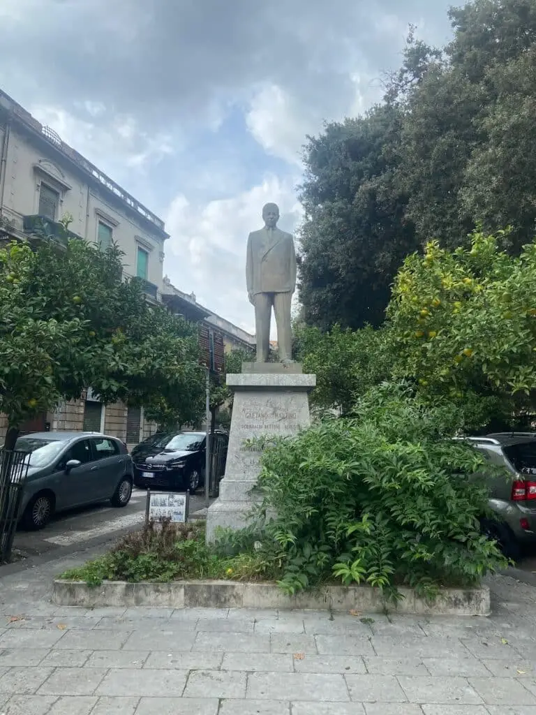 Statua in città con alberi e auto.